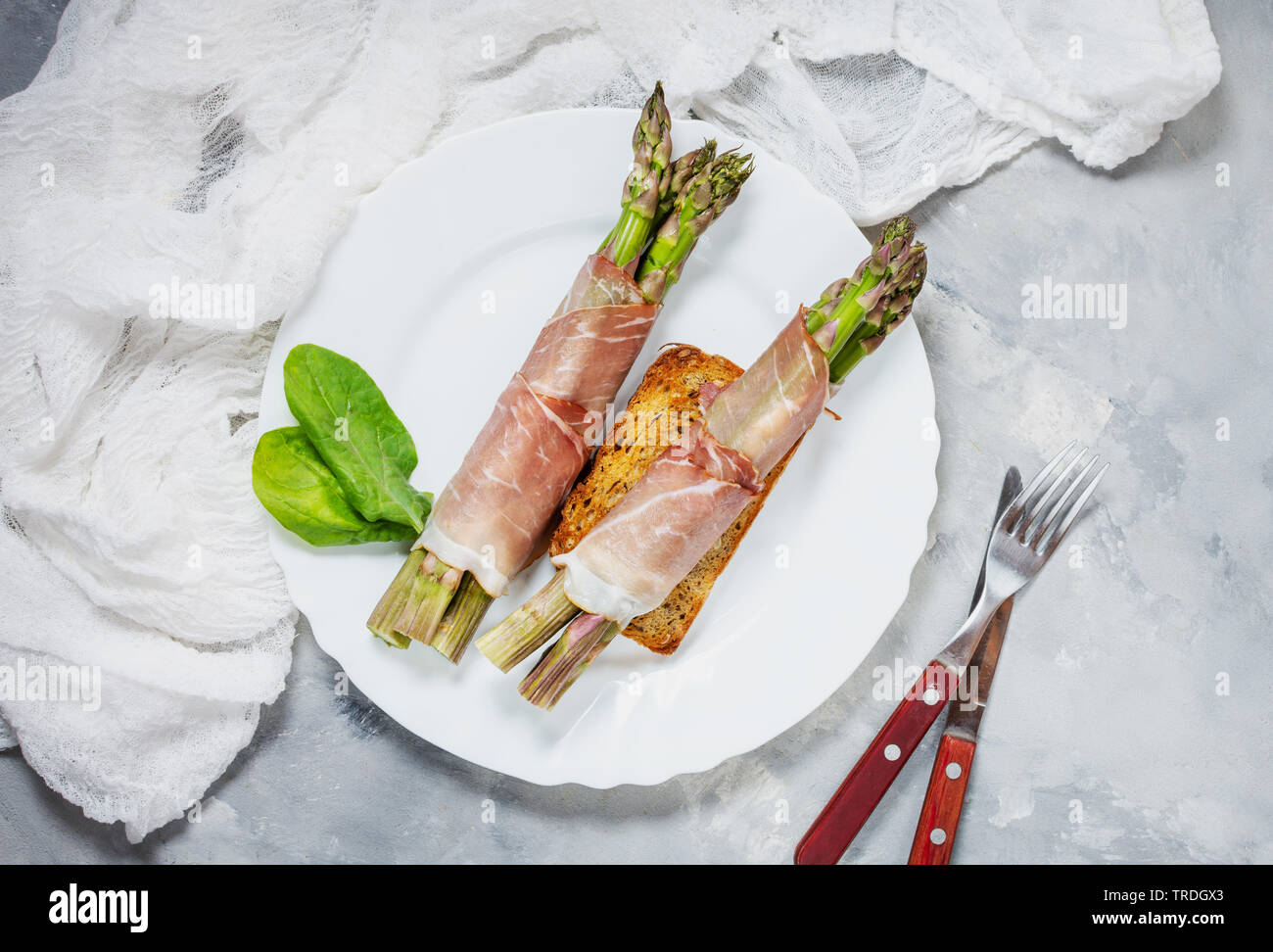 Giovani freschi Asparagi avvolti nel Prosciutto carne su un rustico tavolo in cemento. Vista superiore Foto Stock