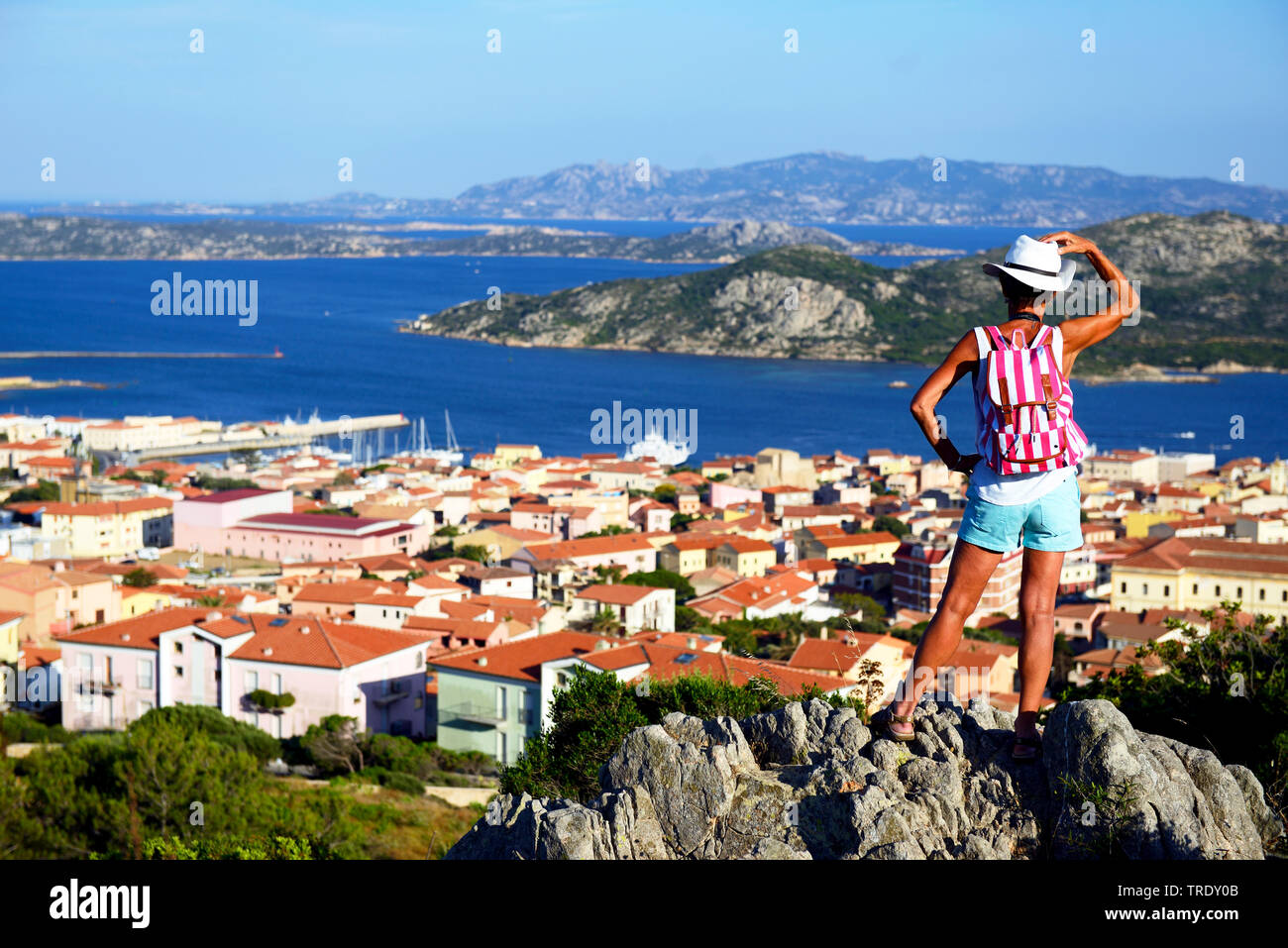 Turista femminile in piedi su una roccia e guardando alla città costiera, l'arcipelago della Maddalena, Italia, Sardegna, Palau Foto Stock