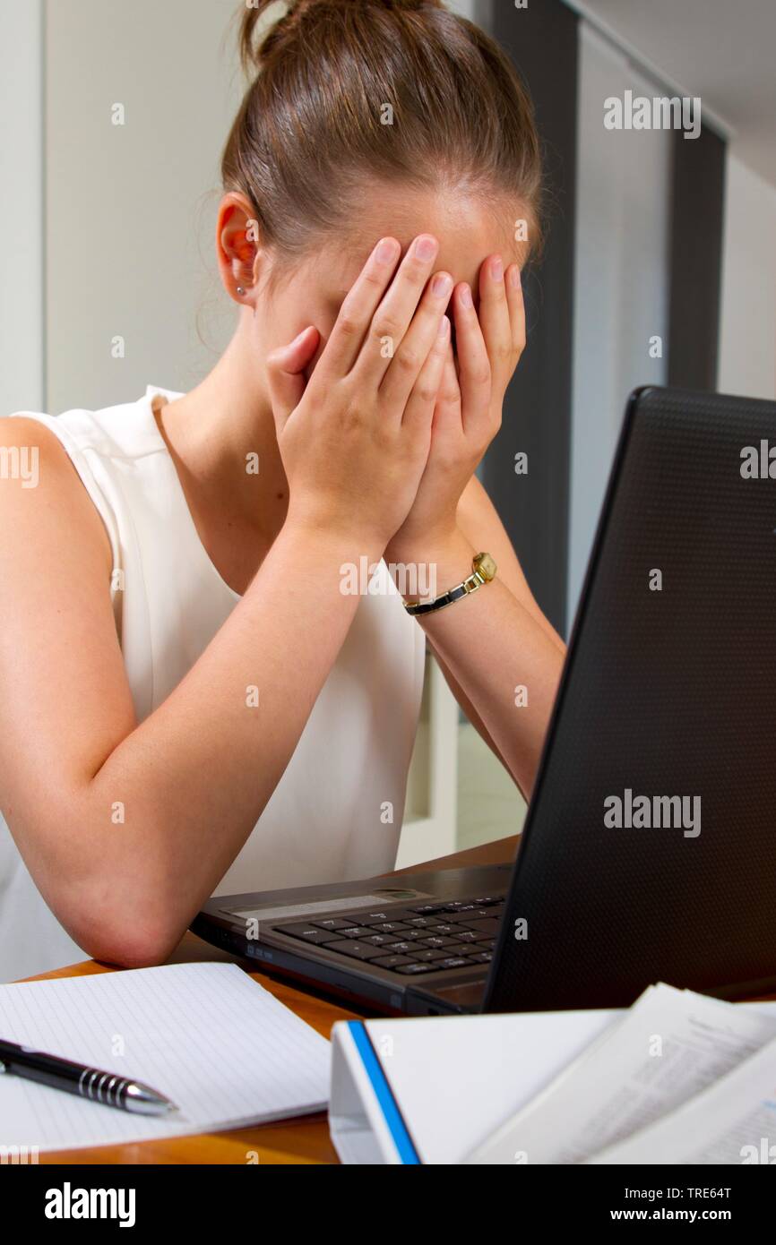 Ritratto di una giovane donna disperato a una scrivania, che copre il volto con le mani Foto Stock