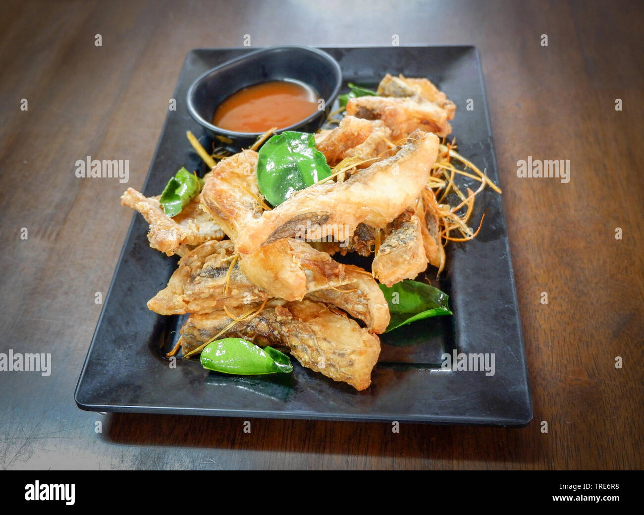 Tilapia fritto croccante di pesce cotto con erbe di erba di limone foglie di combava e salsa sul tavolo Foto Stock