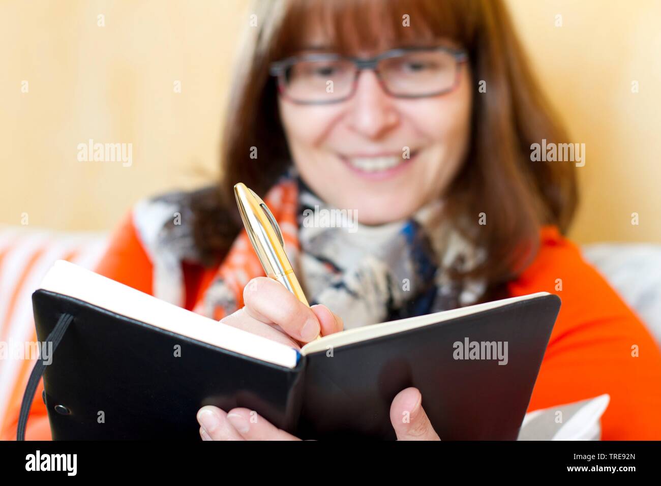 Donna di mezza età con i capelli rossi con gli occhiali seduto su un divano iscritto nel suo notebook Foto Stock