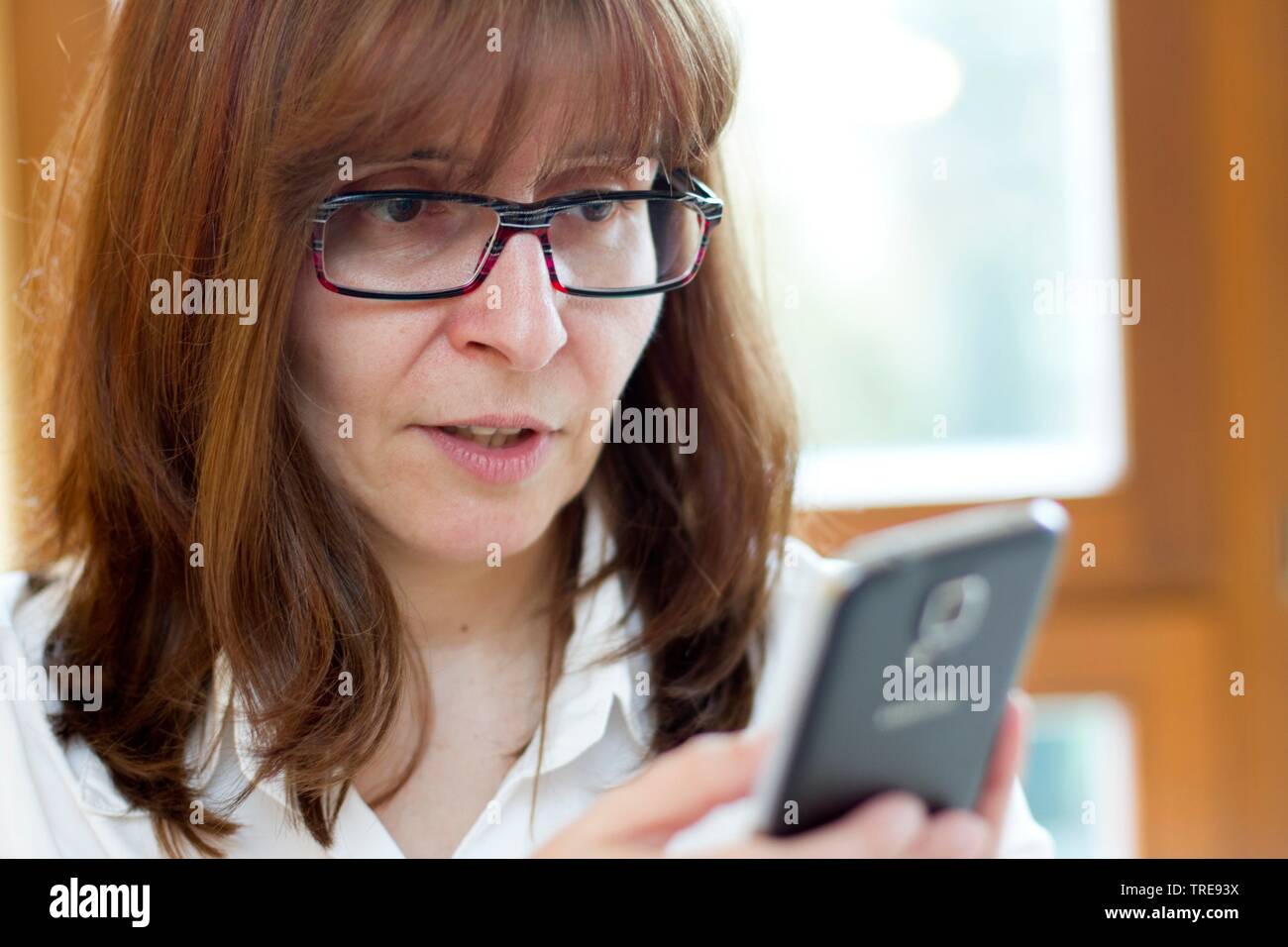 Donna di mezza età con i capelli rossi che indossano occhiali guardando il suo telefono cellulare Foto Stock