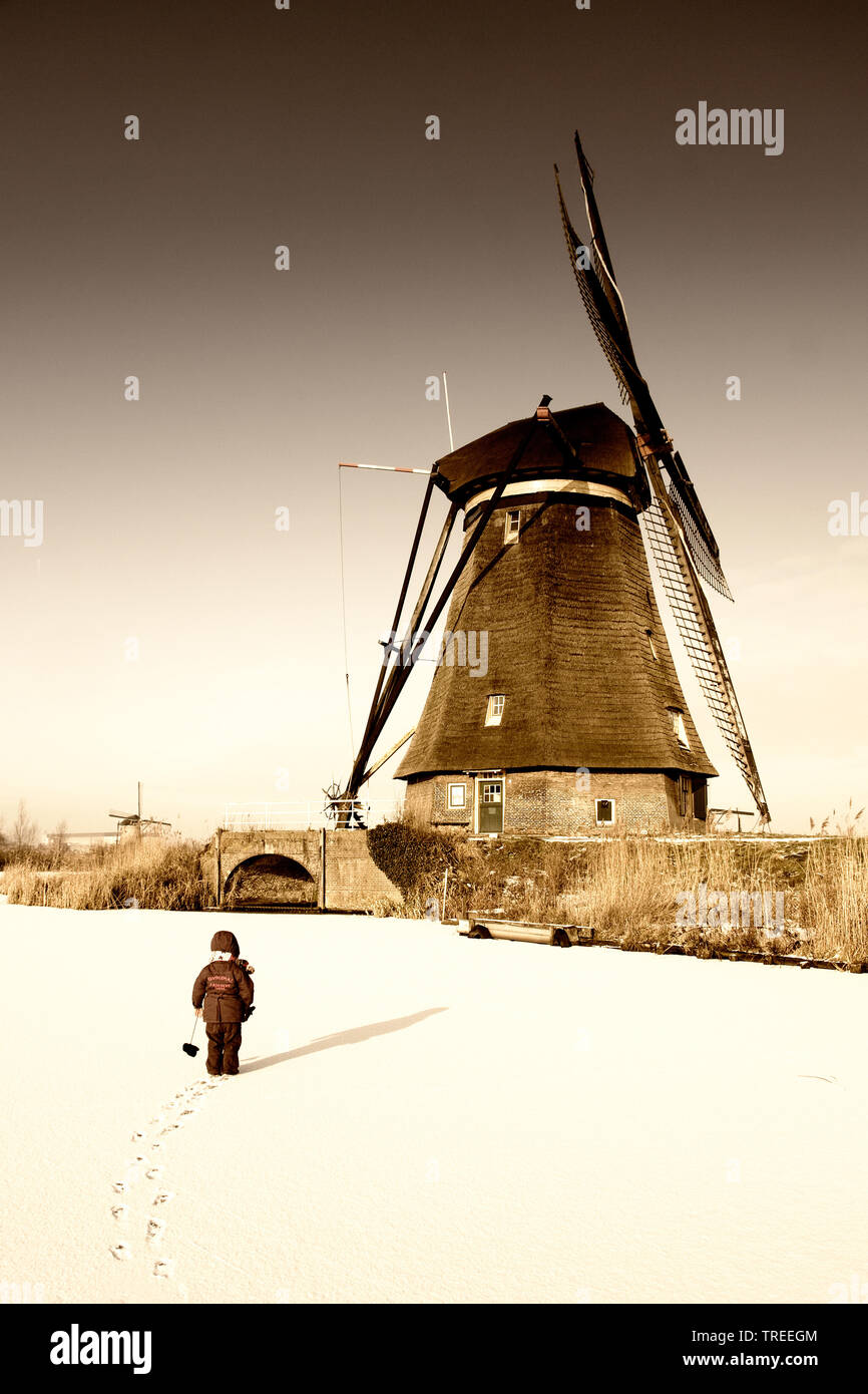 Bambino sul canal congelati nella parte anteriore di un mulino a vento, Paesi Bassi, Kinderdijk Foto Stock