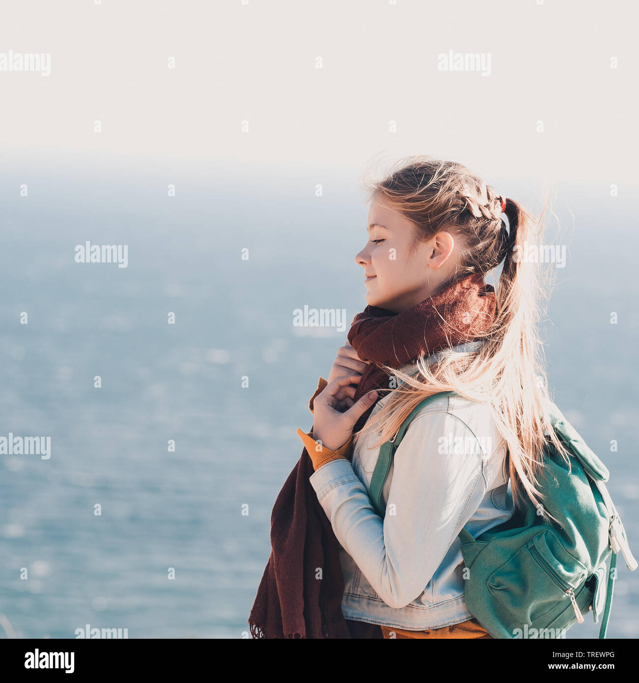 Sorridente ragazza teen 14 16 anni di viaggiare con lo zaino sopra il livello del mare sullo sfondo. Indossa foulard caldo felpa lavorata a maglia e camicia denim Foto stock Alamy