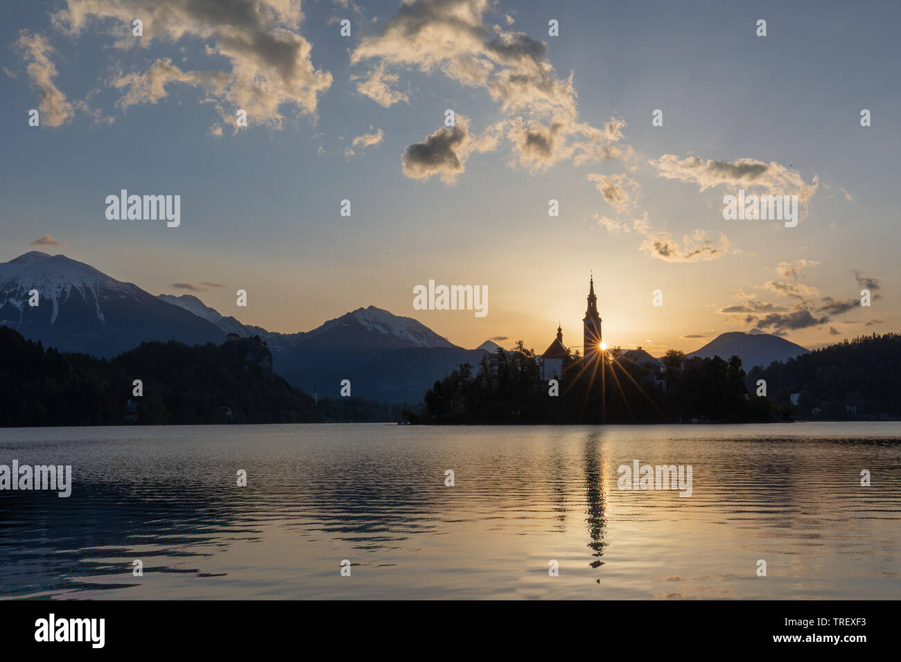 Prime luci dell alba sulla silhouette torre dell Assunzione di Maria la Chiesa al Lago di Bled. Alpi Giulie ancora in ombra in background. Blu cielo con dramati Foto Stock