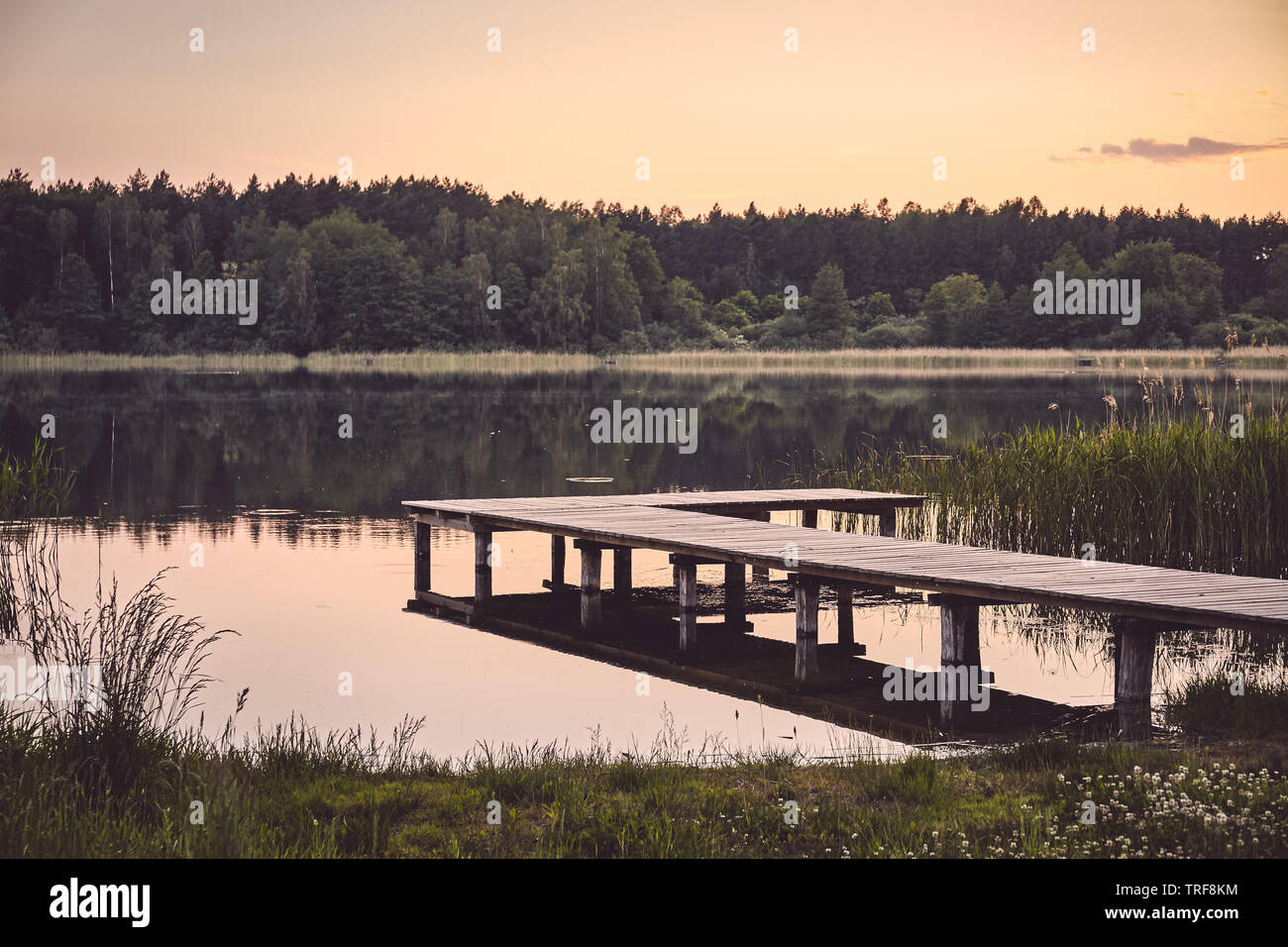 Il molo di legno in corrispondenza di un lago calmo al tramonto, tonificazione del colore applicato. Foto Stock