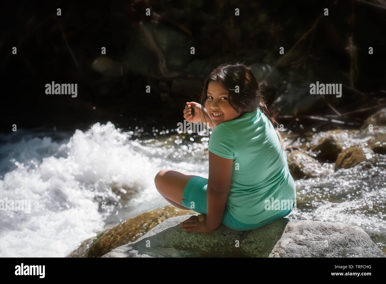Giovane ragazza seduta su una roccia accanto al fiume rapids durante il summer camp giorno di viaggio. Foto Stock