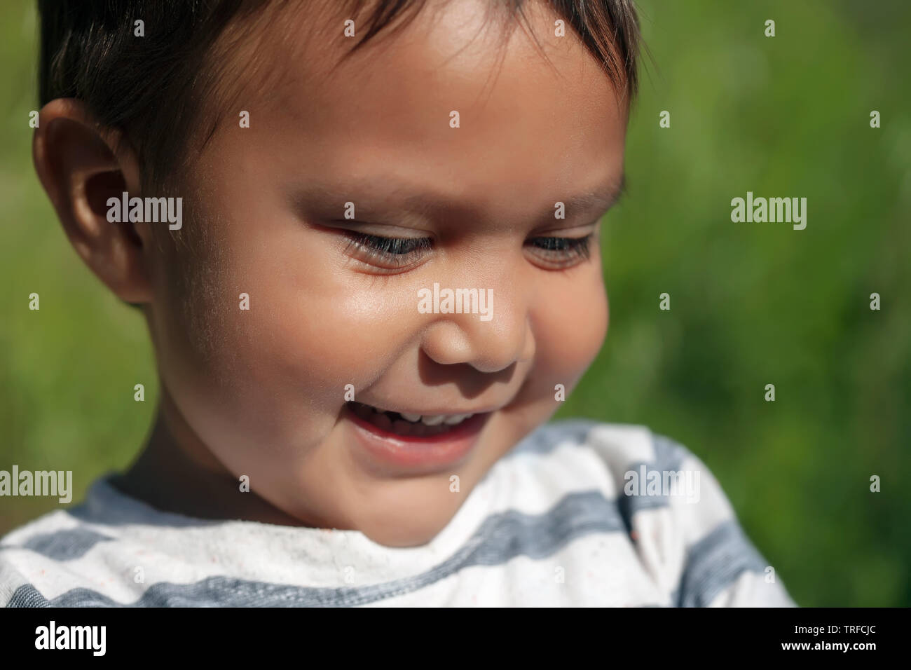 Il viso carino di un ispanico giovane ragazzo sorridente e guardando pensieroso a qualcosa in una giornata di sole. Foto Stock