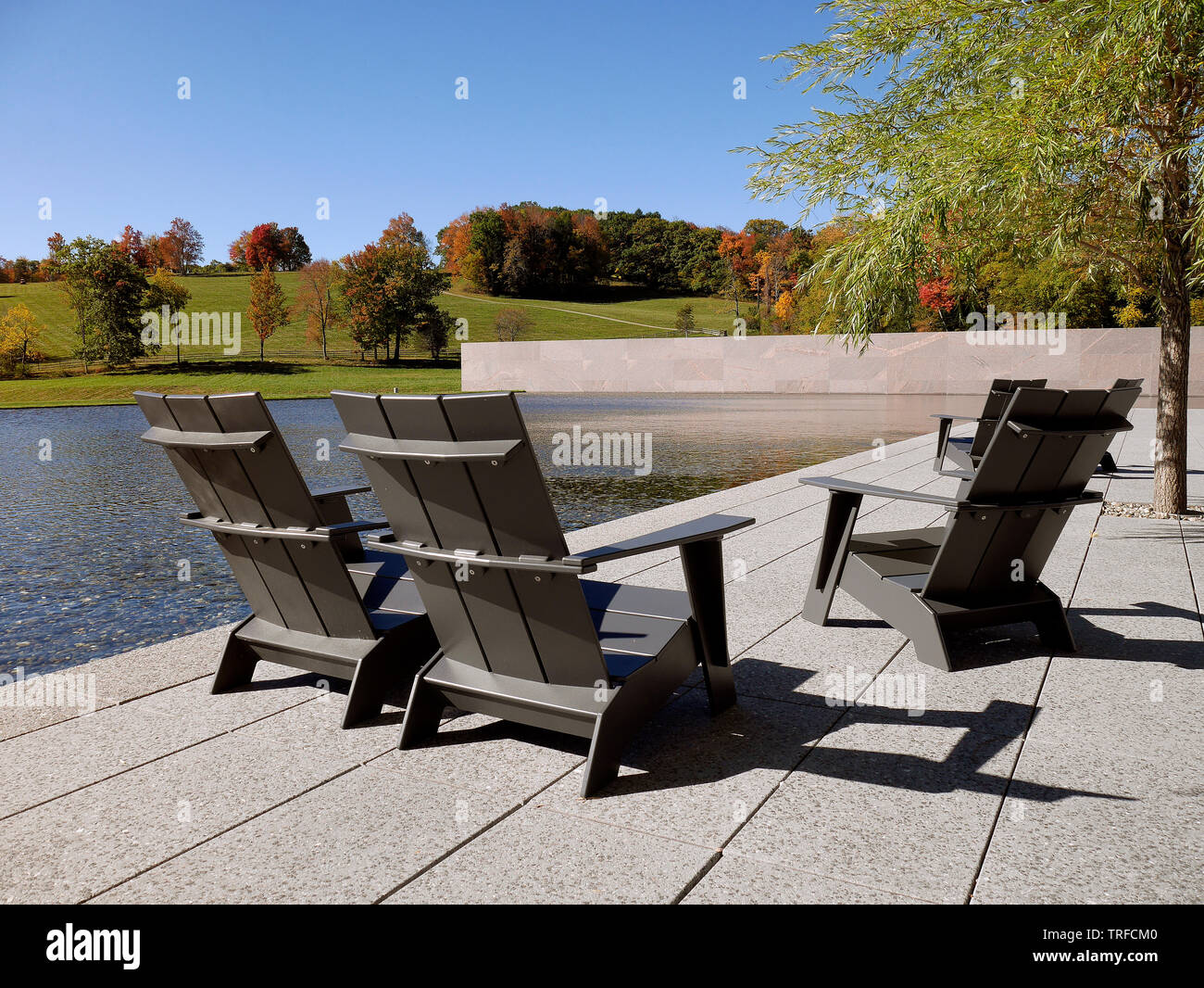 Rilassante ambiente a bordo piscina con tre classiche sedie Adirondack disposte per il massimo comfort. Le linee pulite e l'acqua blu serena creano un'atmosfera estiva di lusso. Foto Stock