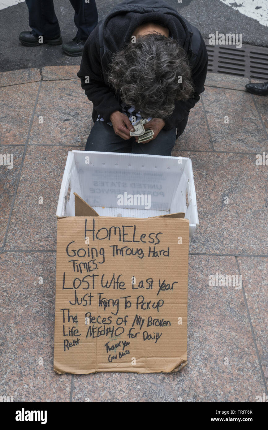 Senzatetto mendicante conta le sue donazioni sulla 42nd Street nel centro di Manhattan, New York. Foto Stock