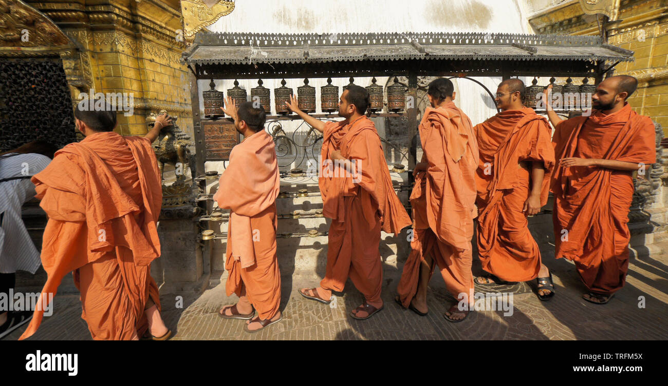 I monaci buddisti in arancione vesti la filatura ruote della preghiera in corrispondenza di una nicchia dorato del grande stupa di Swayambhunath tempio buddista, Kathmandu, Kathmandu Vall Foto Stock