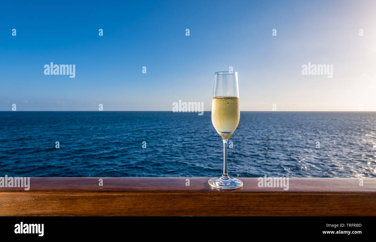 Un bicchiere di champagne su una ringhiera di legno di una nave da crociera. Sullo sfondo del mare. Foto Stock