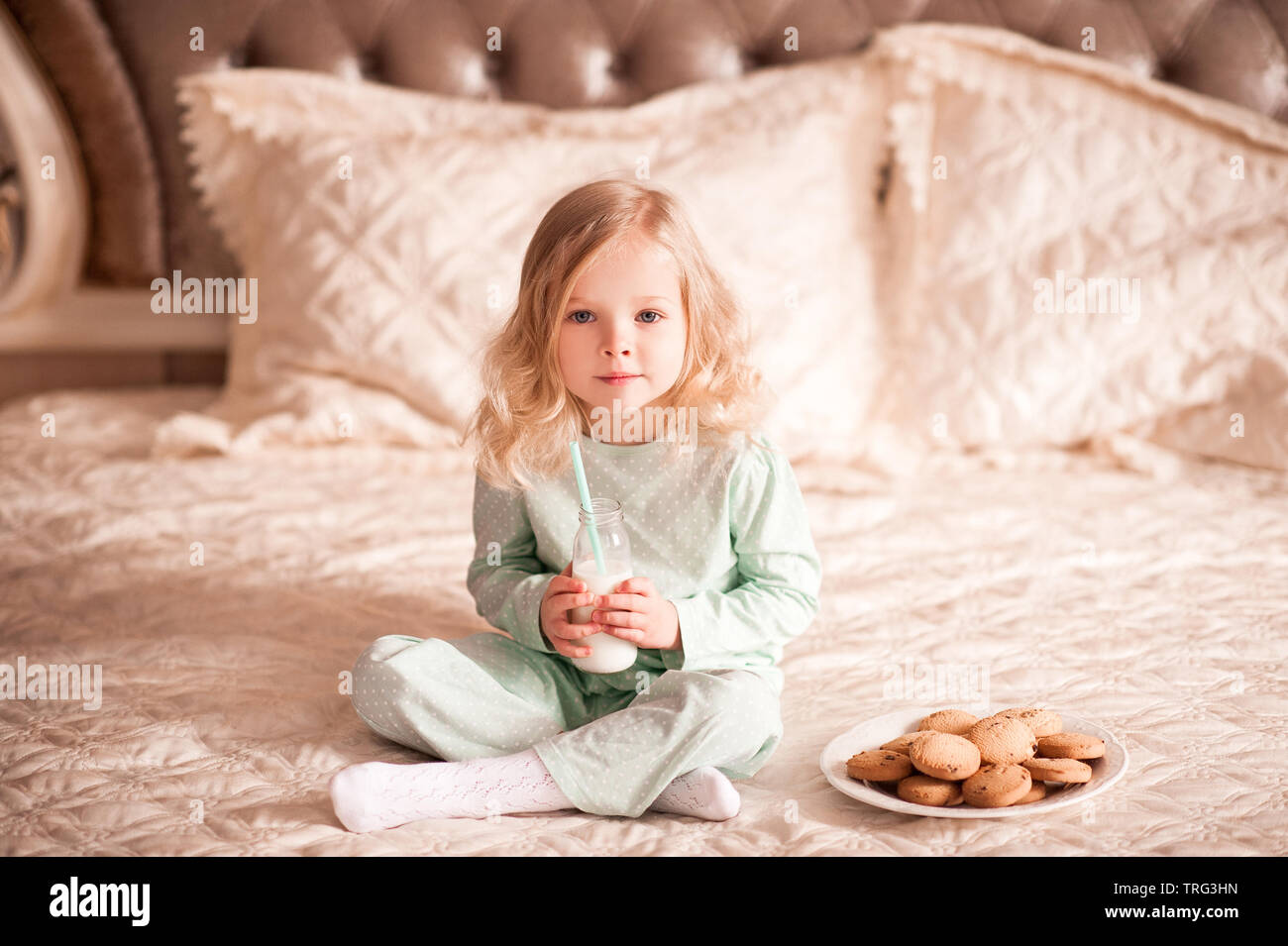 Carina ragazza Bambini 3-4 anno olo avente la colazione a letto. Il latte da bere e mangiare i biscotti fatti in casa. Buona mattina. Foto Stock