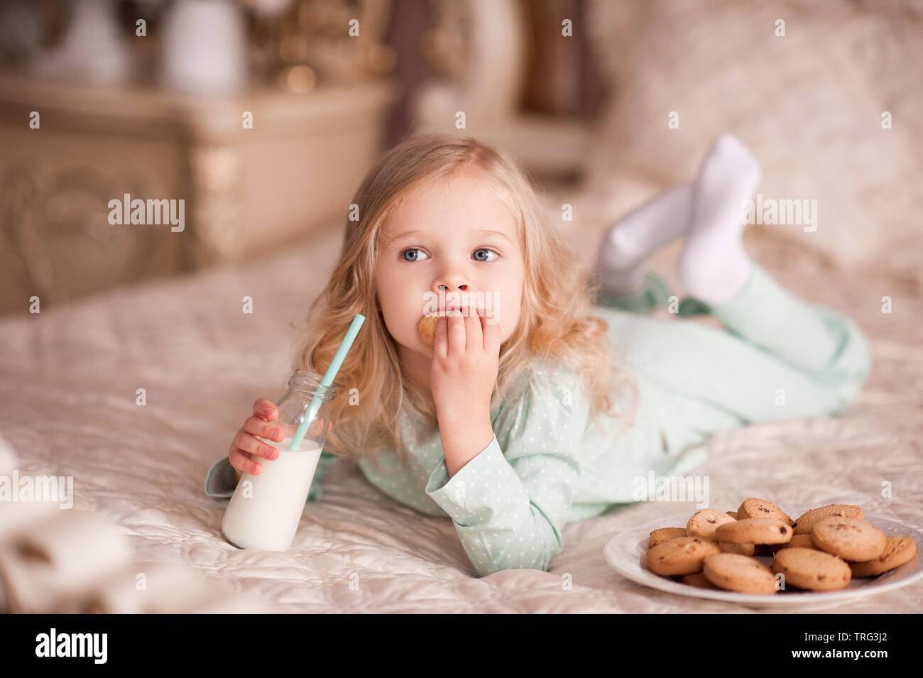 Funny Girl 3-4 anni i cookie di mangiare e di bere latte nel letto. Buona mattina. La prima colazione. Foto Stock