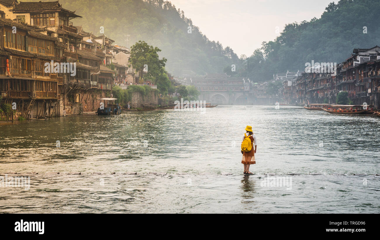 Donna su pietre di macerazione ponte sul tuo fiume Juang sembra camminare sull'acqua in Fenghuang antica città in Cina Hunan Foto Stock