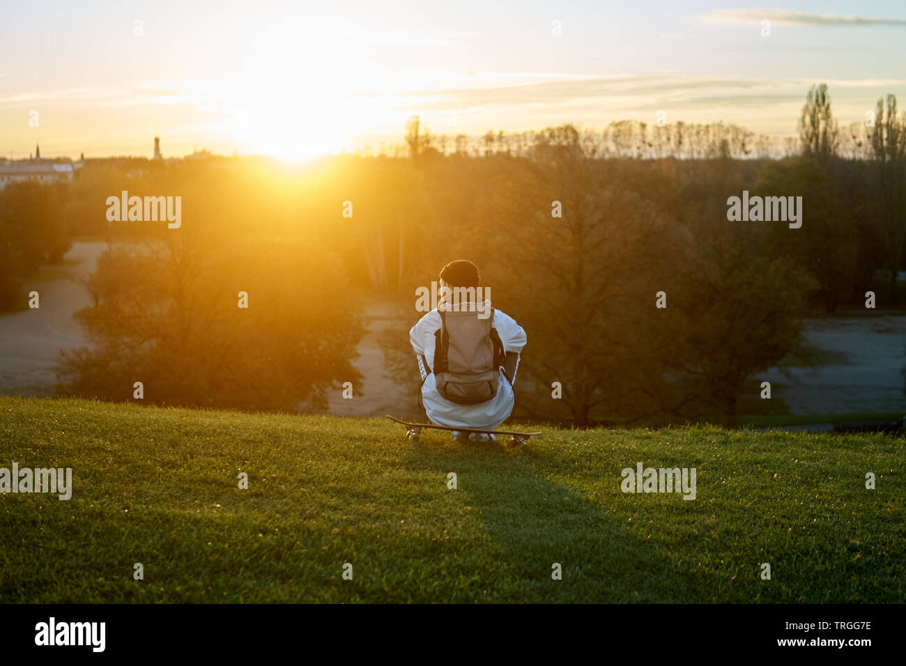Questo stile di vita immagine mostra un giovane uomo seduto sul suo skateboard. La scena è illuminata dalla luce calda del sole al tramonto. Foto Stock