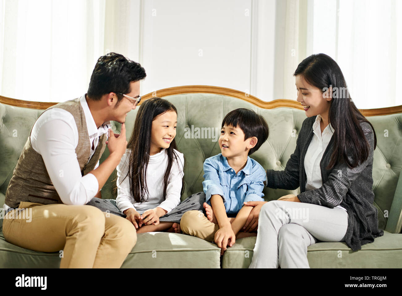 Giovani asiatici il padre e la madre e due bambini seduti sul lettino in chat nel salotto di casa Foto Stock