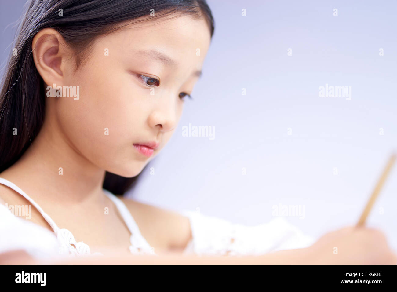 La faccia di una piccola ragazza asiatica con lunghi capelli neri di scrittura o di disegno, close-up shot. Foto Stock