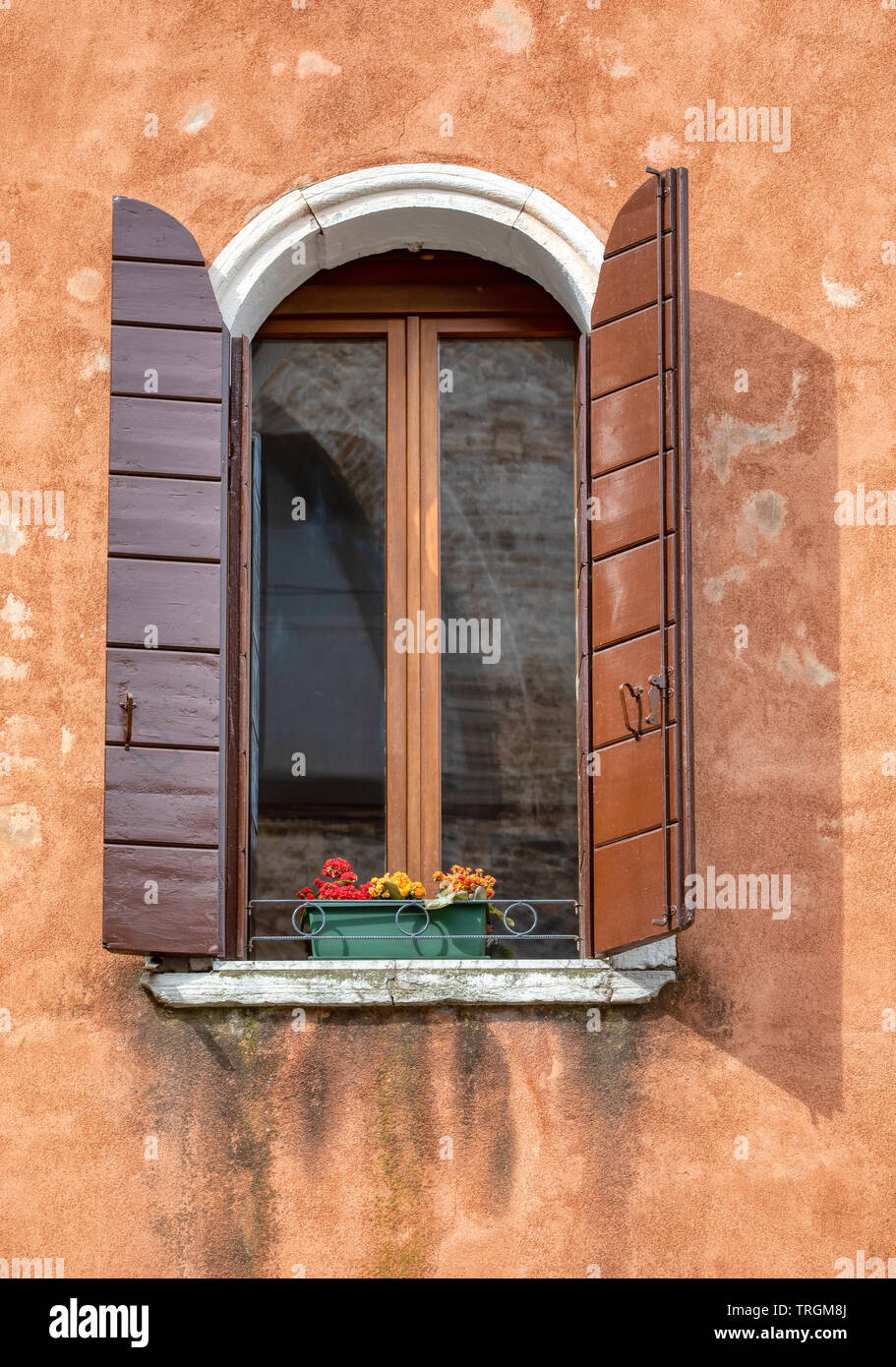 Fotografia di un lone weathered, marrone finestra contro un arancione sbiadito parete in gesso. Prese a Venezia, Italia. Foto Stock