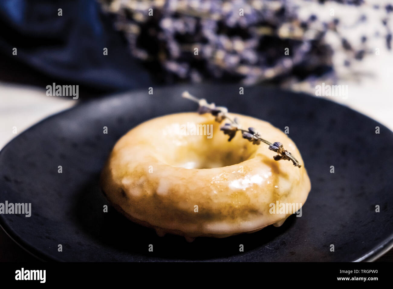 Lavanda lucido ciambella con zucchero semplice smalto e lavanda essiccata sul Fiore nero Piastra in ceramica con profumo di lavanda dietro Foto Stock