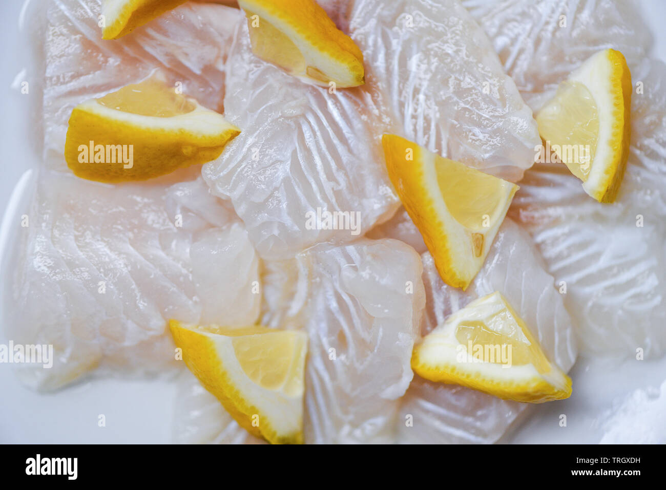 Fresh raw fish fillet piece with lemon on white plate background / Close up pangasius dolly fish meat Foto Stock