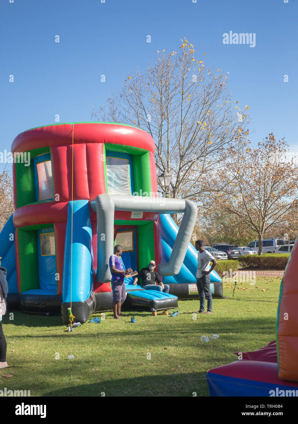 Variopinto jumping castello per bambini su un verde prato erboso all'aperto presso un mercato con uomini adulti vicino su una soleggiata giornata autunnale a Stellenbosch Foto Stock