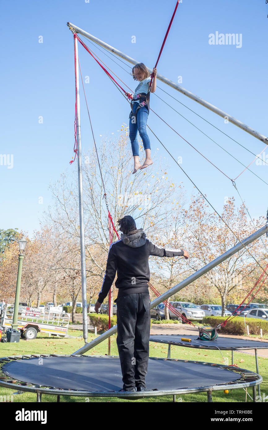 Giovane ragazza caucasica o bambino sospesa a mezz aria su un trampolino con fascette attaccate e un helper maschio verso il basso al di sotto di chi sta assistendo a un mercato Foto Stock