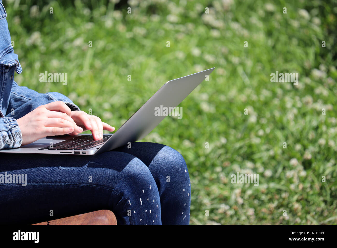 Ragazza seduta con un computer portatile su un banco in un parco d'estate. Mani femminili su una tastiera, il concetto di studente, lavorando all'aperto, imprenditrice, communi online Foto Stock