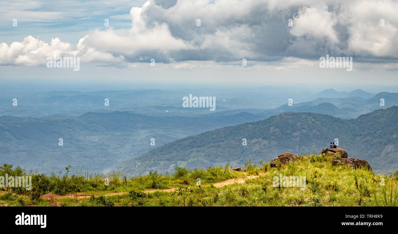 Due persona seduta sulla roccia per un ampio panorama con hill, cielo blu e nuvole bianche. Foto Stock