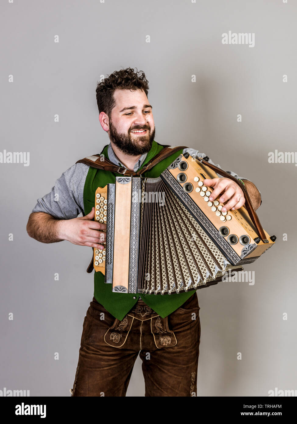 Giovane uomo con barba nera e pantaloni in pelle e il costume tradizionale  e la fisarmonica è in posa di fronte a uno sfondo grigio Foto stock - Alamy