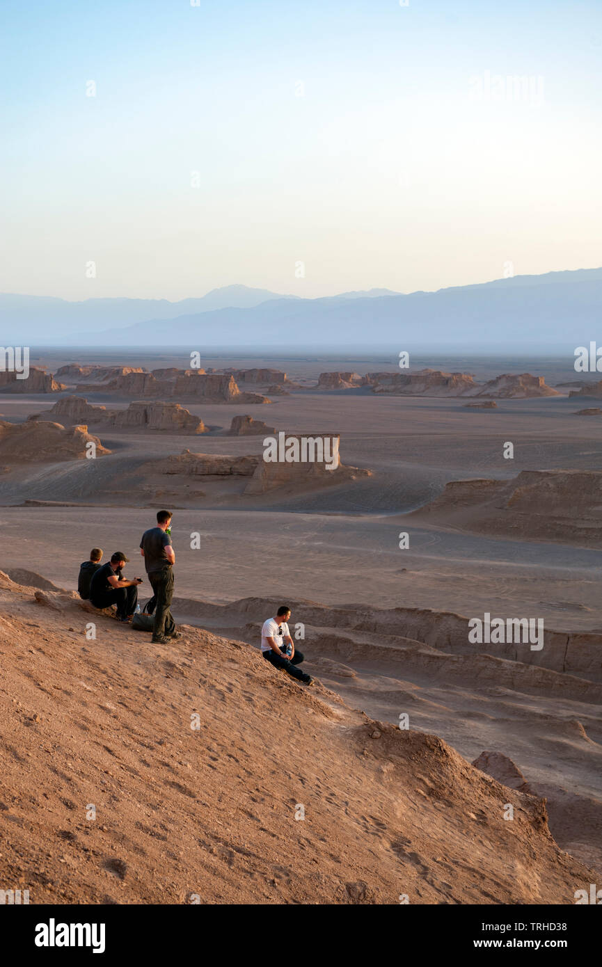 I turisti guardano il sole tramontare sugli yardangs nel deserto LUT a Shahad, Iran. Conosciuta come le malghe in Iran, gli yardangs sono formazioni geologiche. Foto Stock
