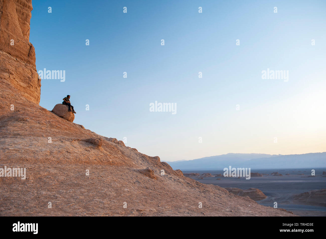 Un turista guarda il sole tramontare sugli yardangs, conosciuti come kuluts in Iran, nel deserto di LUT a Shahad, Iran. Foto Stock