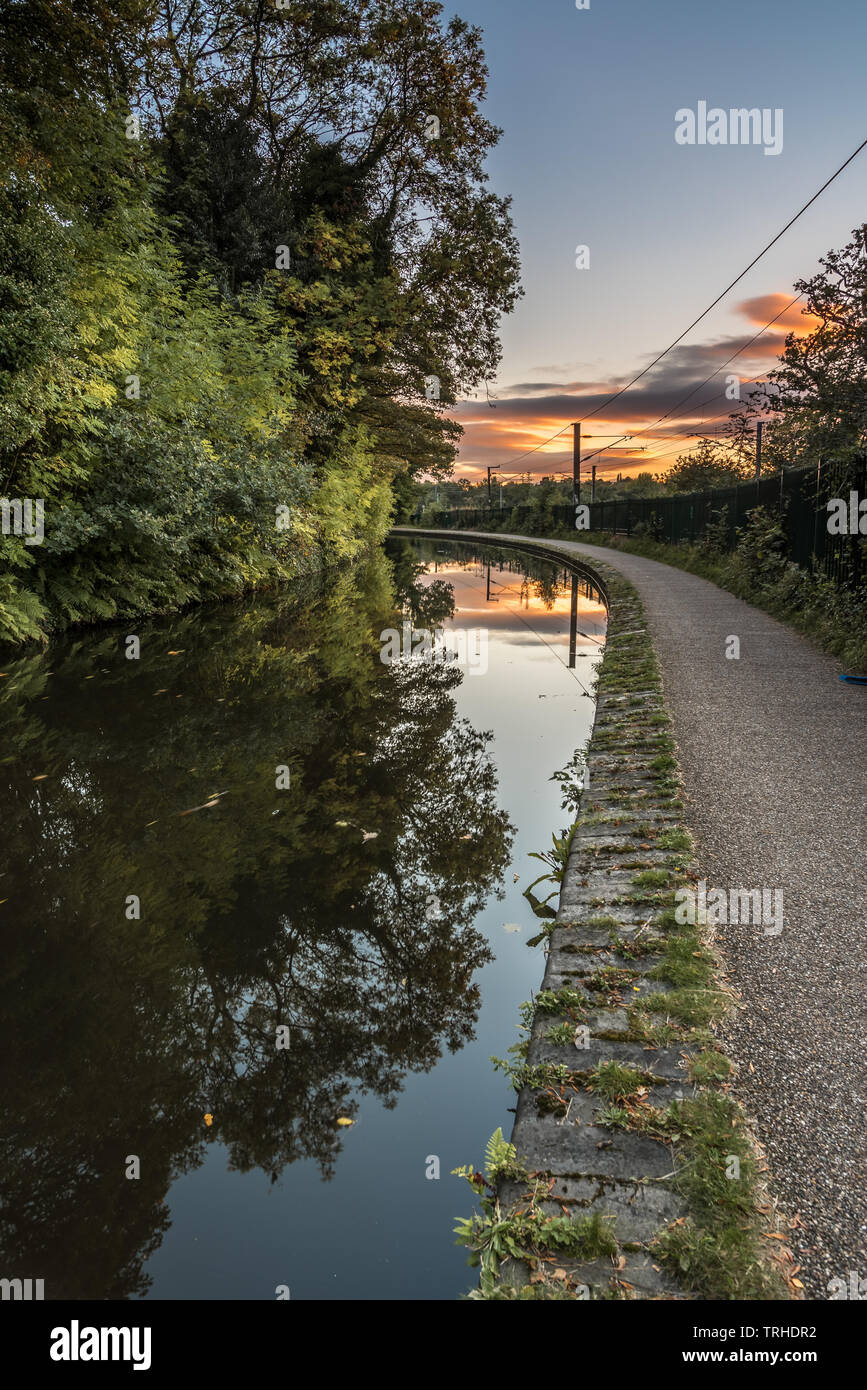 Worcester a Birmingham canal, in Inghilterra, Regno Unito. Il rosso e l'arancione del sole al tramonto è perfettamente riflessa nella molto calme acque del canale Foto Stock