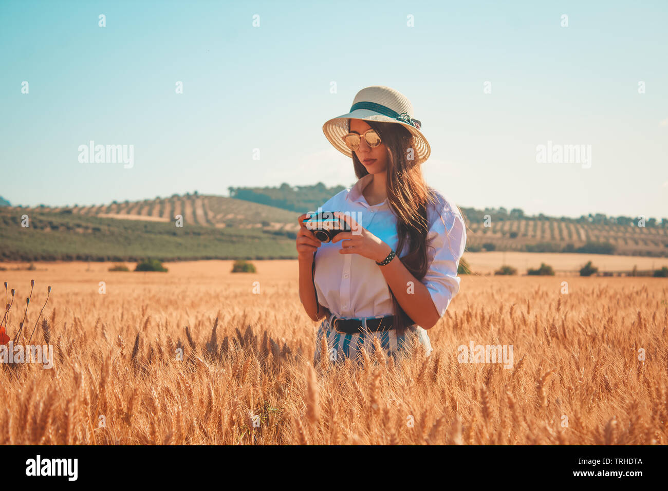Una giovane donna di trascorrere del tempo all'aperto e prendendo foto con un vintage foto fotocamera e alla moda da indossare occhiali da sole e cappello per il sole Foto Stock