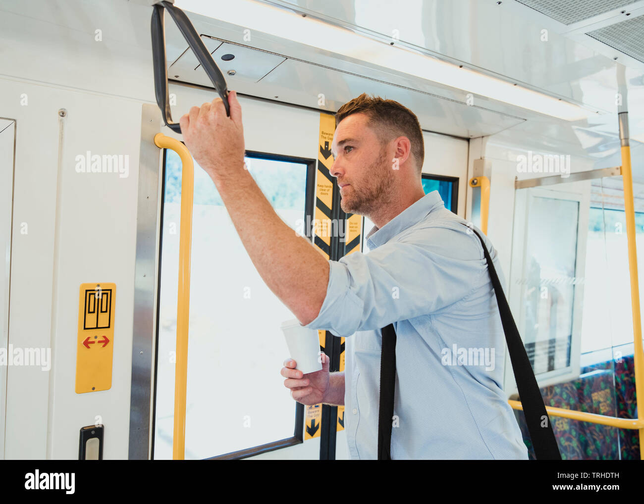 Una vista laterale colpo di un mid-imprenditore per adulti in piedi su un treno pendolari, egli è in possesso di una tazza di caffè. Foto Stock