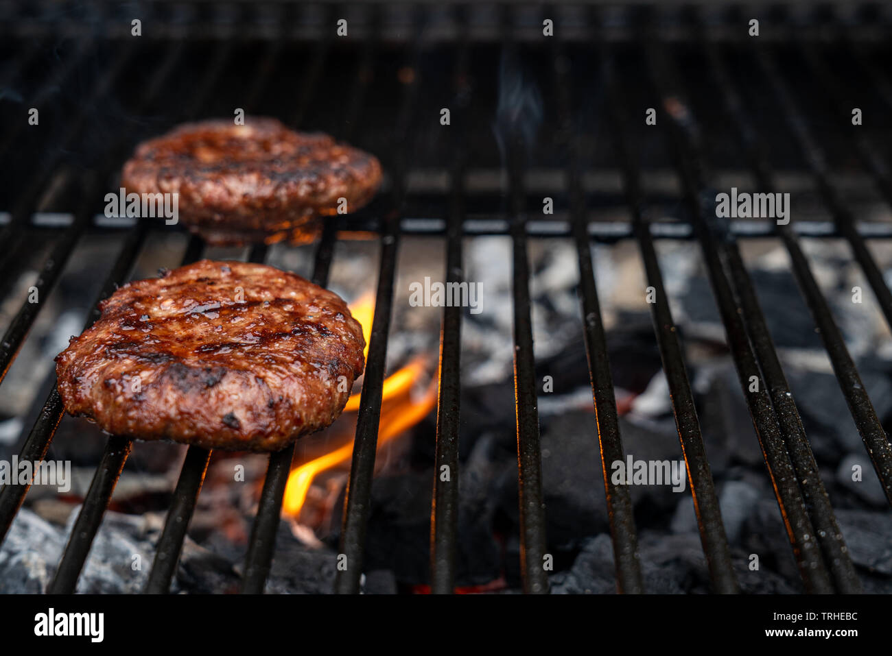 Fatta in Casa succosa hamburger di manzo alla griglia su il barbecue. Fire dal carbone al di sotto della hamburger. copia spazio per il testo Foto Stock