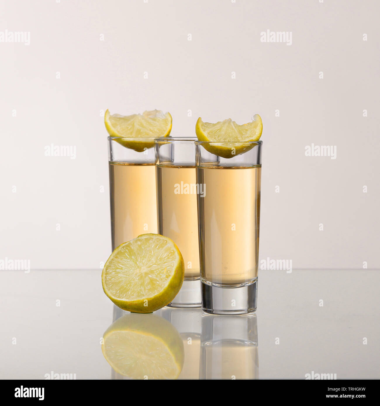 Tre d'oro tequila scatti con calce su sfondo bianco Foto Stock