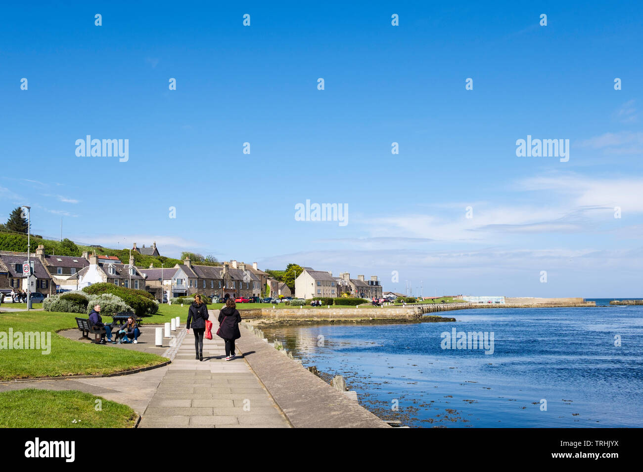 Vista lungo la passeggiata lungomare con due donne visitatore occasionale accanto al fiume Lossie bocca su di Moray Firth coast. Lossiemouth, murene, Scozia, Regno Unito, Gran Bretagna Foto Stock