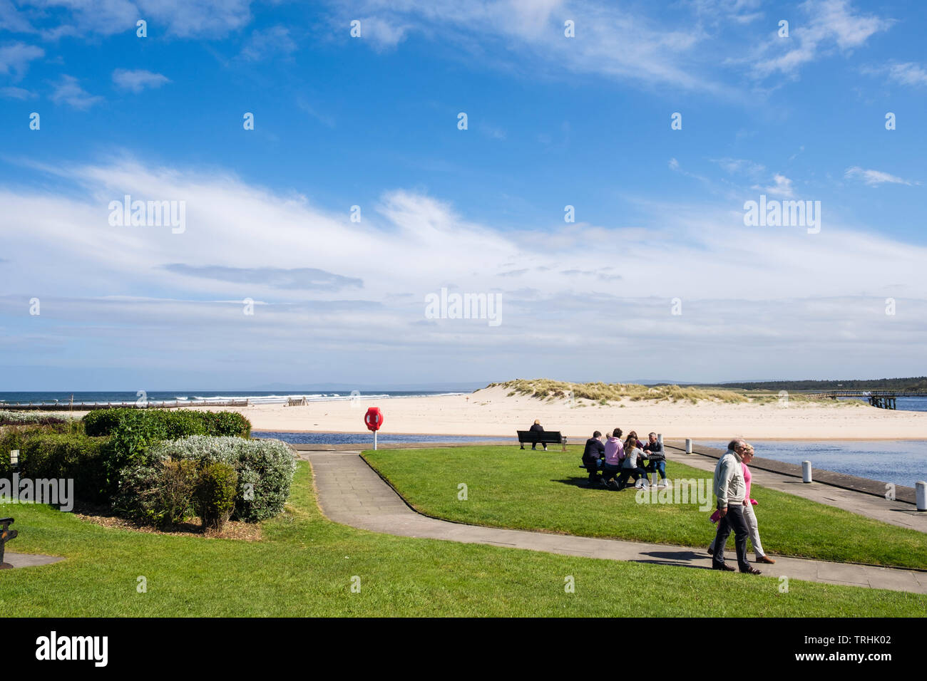 La gente che camminava sul lungomare accanto al fiume Lossie bocca con sabbia di spiaggia a est sul Moray Firth coast. Lossiemouth Moray Scozia UK Gran Bretagna Foto Stock