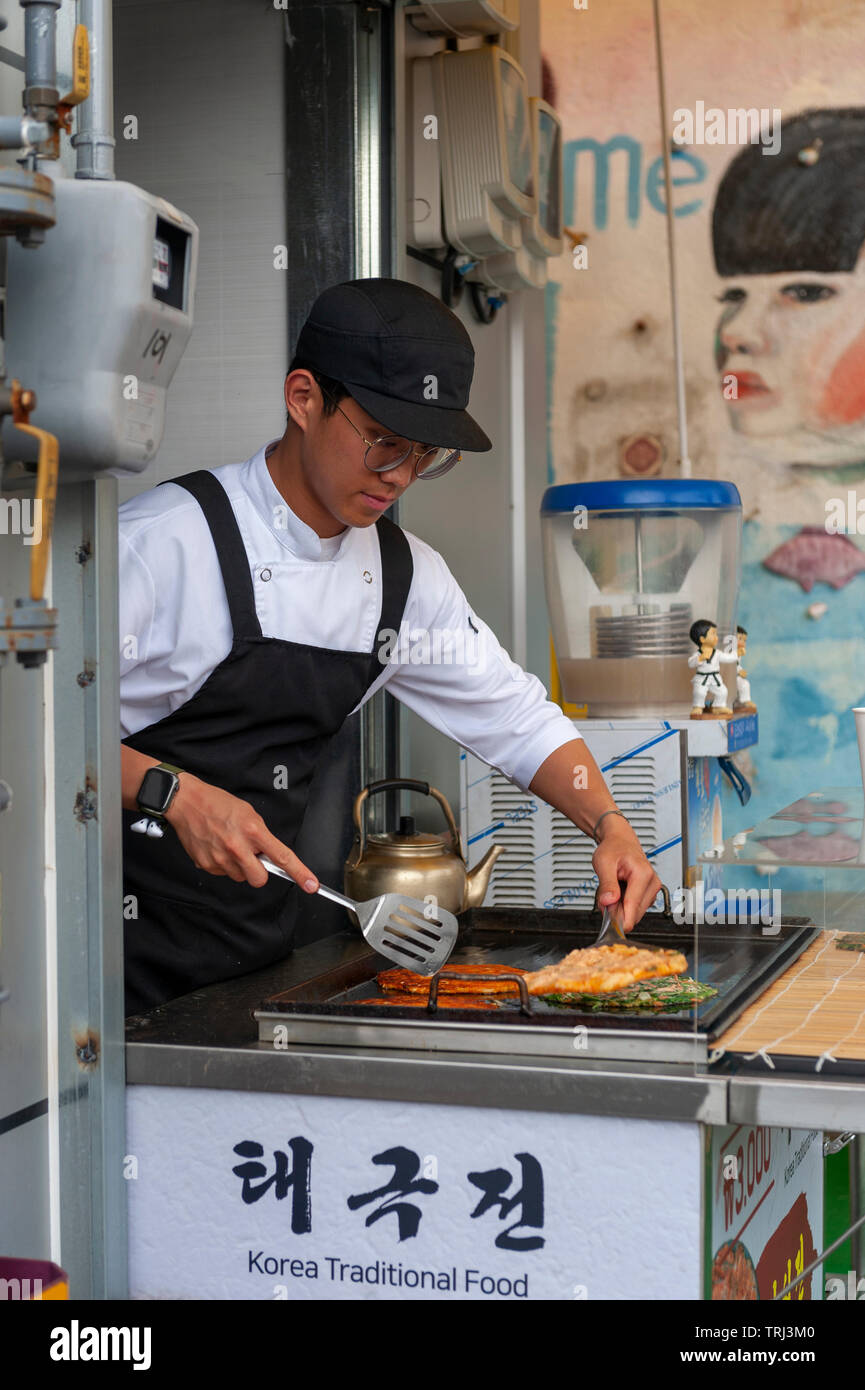 Giovane venditore Buchimgae cottura o coreano pancake, Coreano Tradizionale cibo, a un cibo stallo nella cultura Gamcheon Village di Busan, Corea del Sud Foto Stock