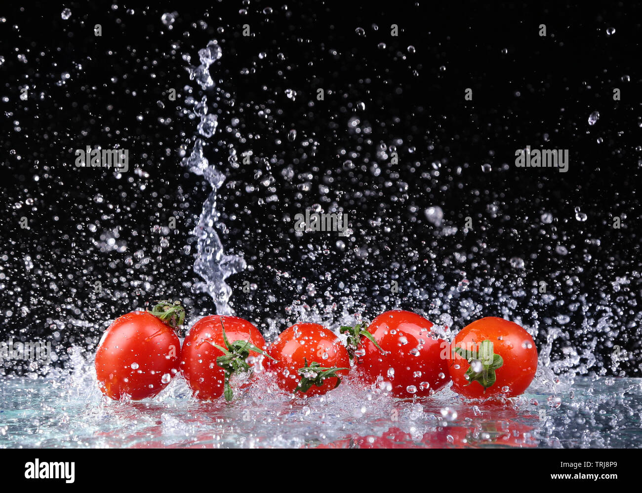 Studio shot con congelare il movimento di pomodori ciliegia in acqua splash su sfondo nero Foto Stock