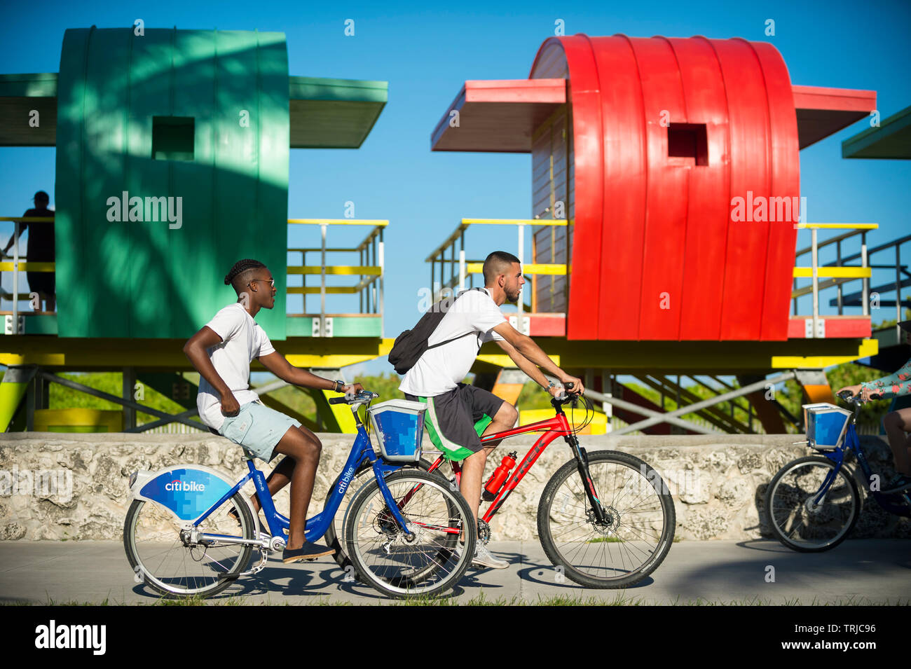 MIAMI - Luglio 2017: turisti utilizzando CitiBike bicicletta sistema condividi ride lungo la passeggiata in spiaggia a sud di fronte a una fila di coloratissimi lifeguard torri. Foto Stock