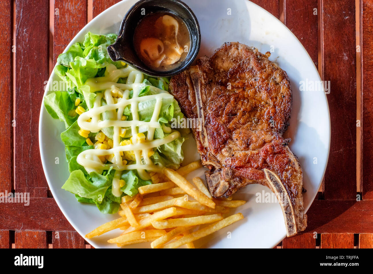 Grigliata di costolette di maiale bistecca ben fatto con le patatine fritte e verdure sulla piastra bianca Foto Stock