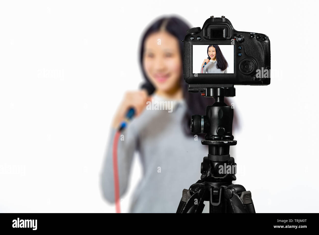 Focus sulla visualizzazione live su telecamera sul cavalletto, ragazza adolescente cantando con microfono immagine sul retro schermo con scena sfocata in background. Teenage vlogger l Foto Stock