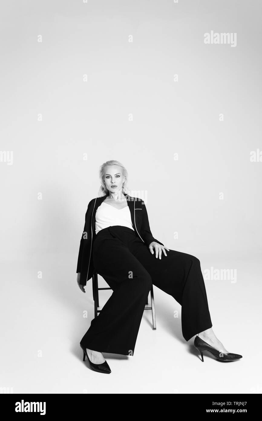 Ritratto in studio di bella donna bionda in un abito nero contro bianco sfondo semplice Foto Stock