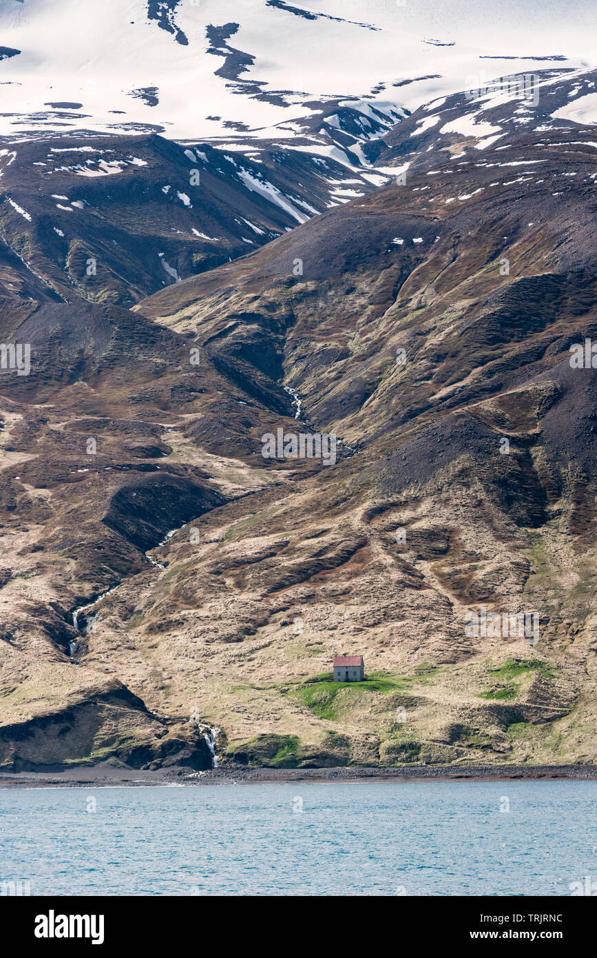 Húsavík, Nord Islanda. Un solitario fattoria sulle rive della baia di Skjálfandi (Skjálfandaflói), sotto le creste innevate di Víknafjöll Foto Stock