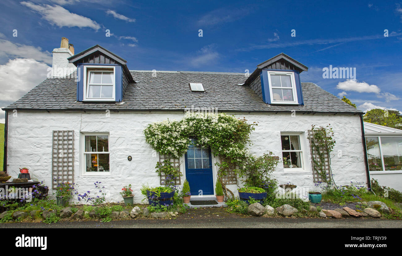 Bianco pittoreschi cottage in pietra con piante rampicanti intorno al portale e finestre dormer sotto il cielo blu a Dornie Scozia Scotland Foto Stock