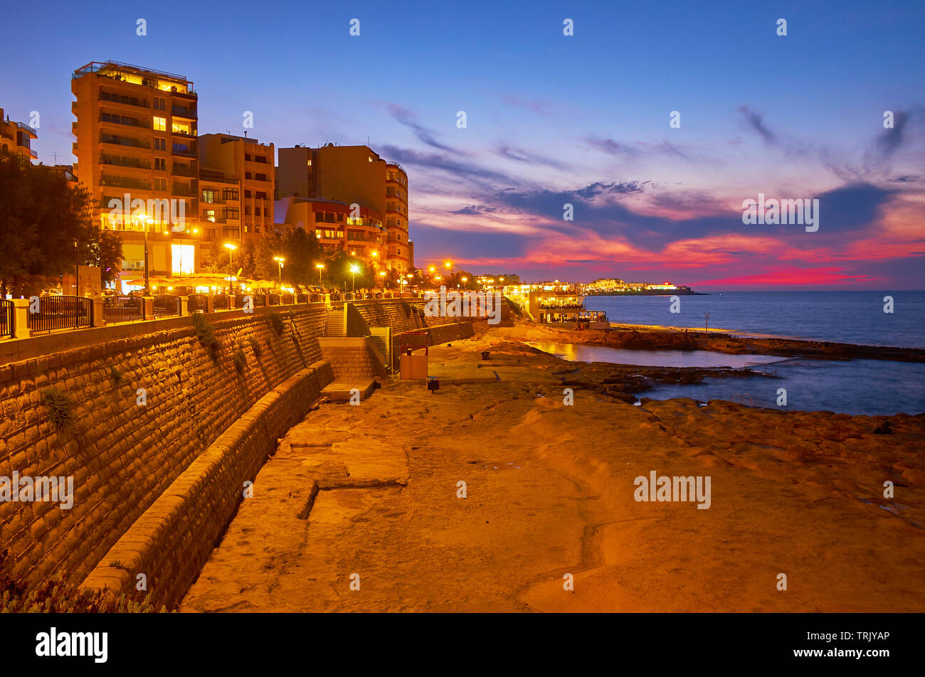 La sera a piedi lungo la passeggiata sul lungomare di Sliema con una vista su moderni quartieri turistici, spiaggia di pietra e cielo al crepuscolo, Malta Foto Stock