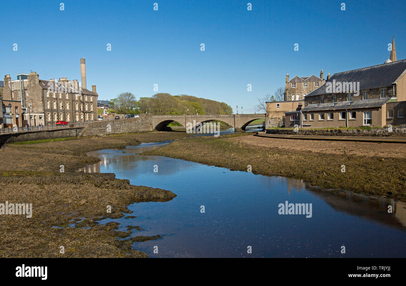 Città di stoppino in Caithness in Scozia con edifici accanto al fiume e al ponte e cielo blu riflessa in acqua calma Foto Stock