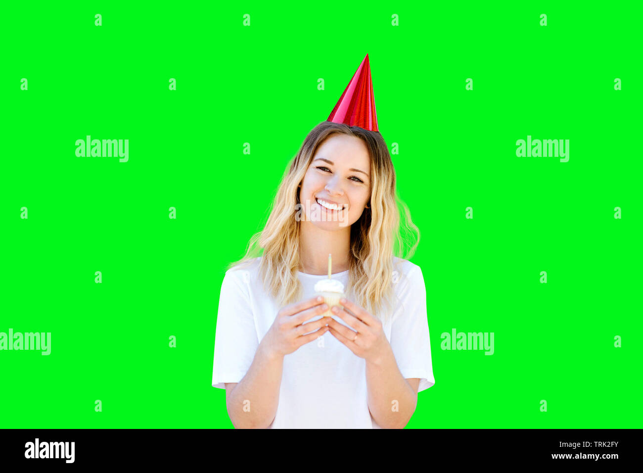 Giovane ragazza caucasica sorrisi mentre tiene un compleanno cupcake e indossando un cappello di compleanno Foto Stock